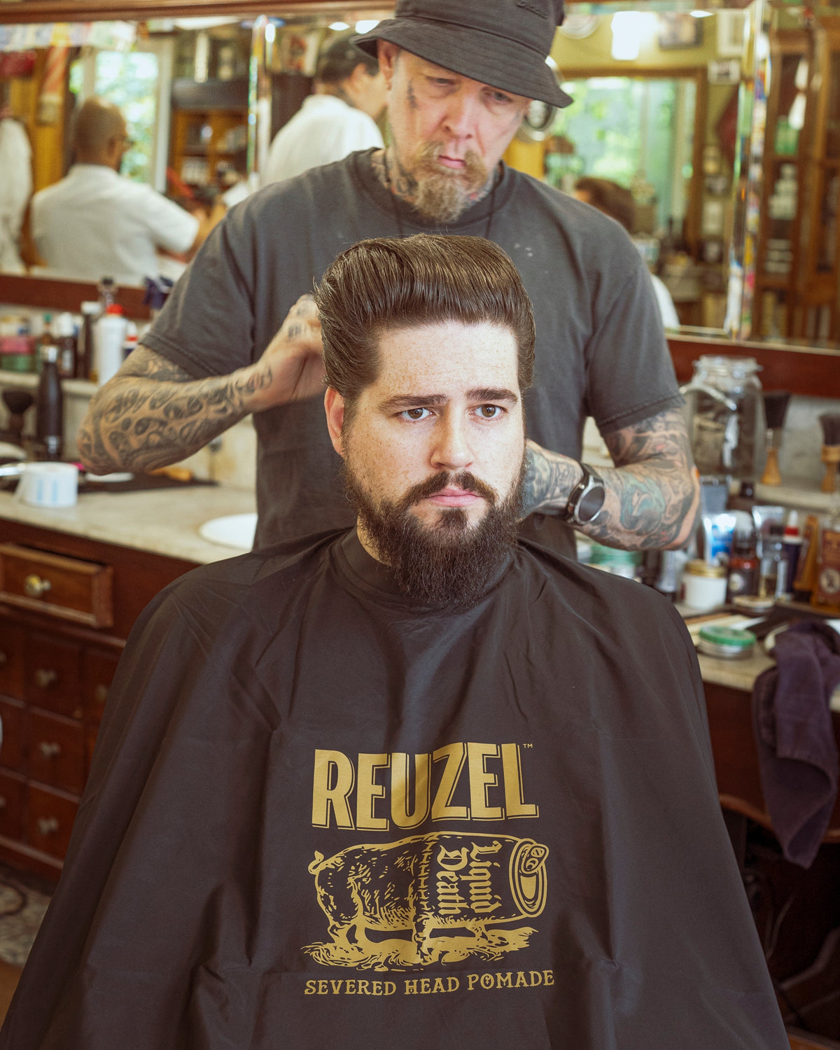 Severed head Reuzel barber cape from REUZEL UK, featuring bold graphic design, used as a stylish hairdressing accessory or merchandise.