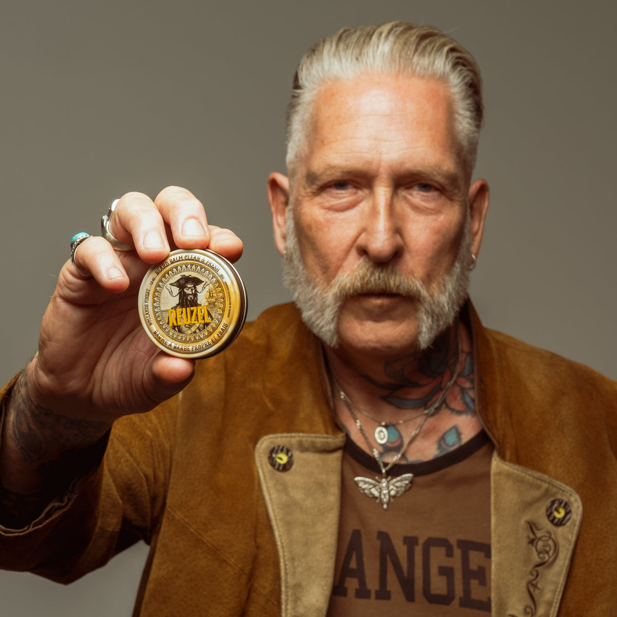 Reuzel UK beard balm with wood and spice scent, featuring a tin container and a grooming brush on a white background.