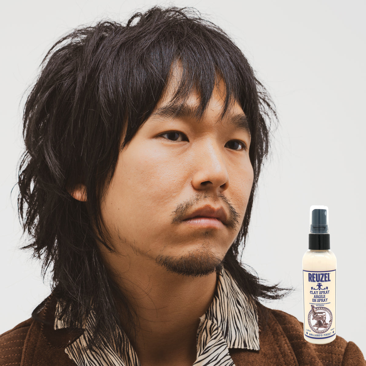 Reuzel UK clay spray bottle with white label and spray nozzle, used for styling and texturizing hair.