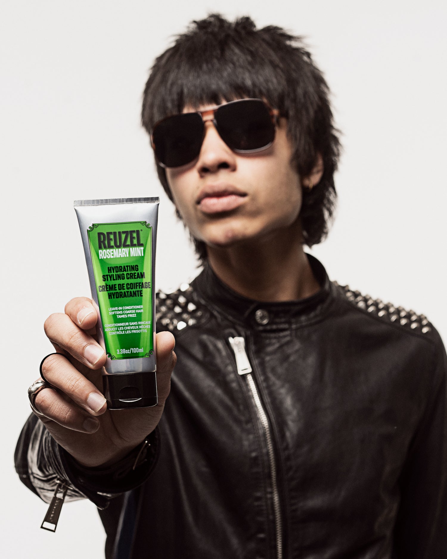 Person holding a tube of Reuzel styling product against a neutral background
