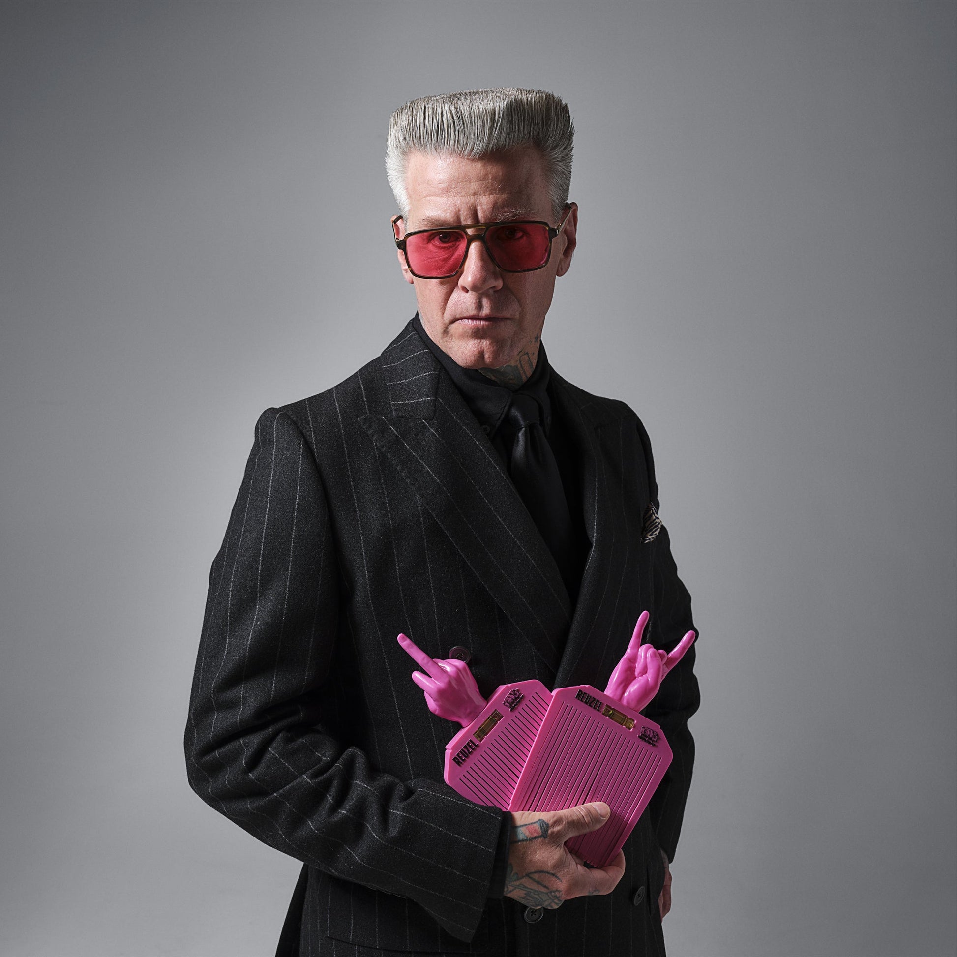 Man in a suit holding Reuzel pink flat top combs against a gray background