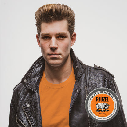 A male model wearing a leather jacked, with hair styled with Orange REUZEL Extreme Hold Matte Pomade jar with orange label, showcasing the product's bold packaging and orange color. 